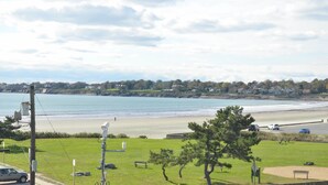Une vue côtière avec une plage, des zones herbeuses et une rangée de maisons en arrière-plan.