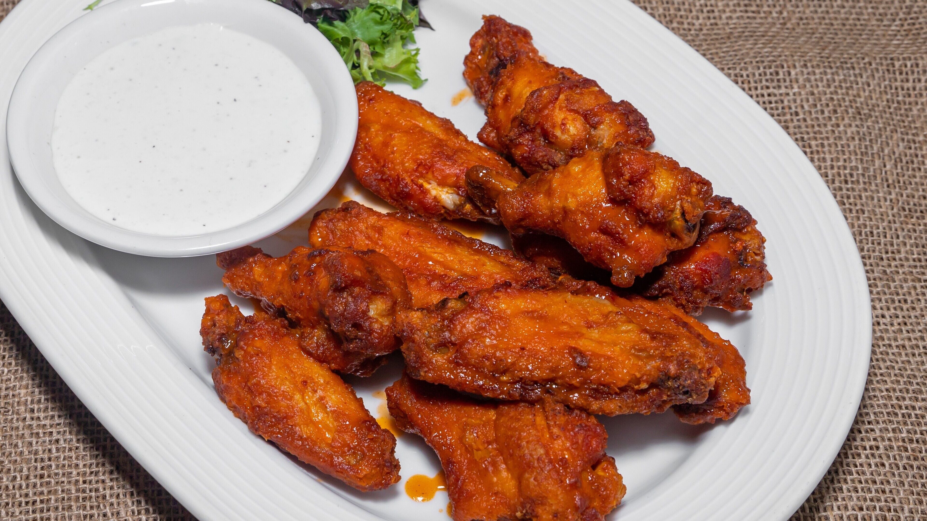 A plate of chicken wings with a side of dipping sauce and a small salad.