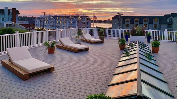 Une terrasse sur le toit, dotée de chaises longues et de plantes en pot, qui offre une vue sur le bord de l’eau, avec des bâtiments en arrière-plan.