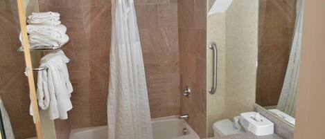 A bathroom with a bathtub, a shower curtain, a towel rack with towels, a handrail, a sink, and a mirror.