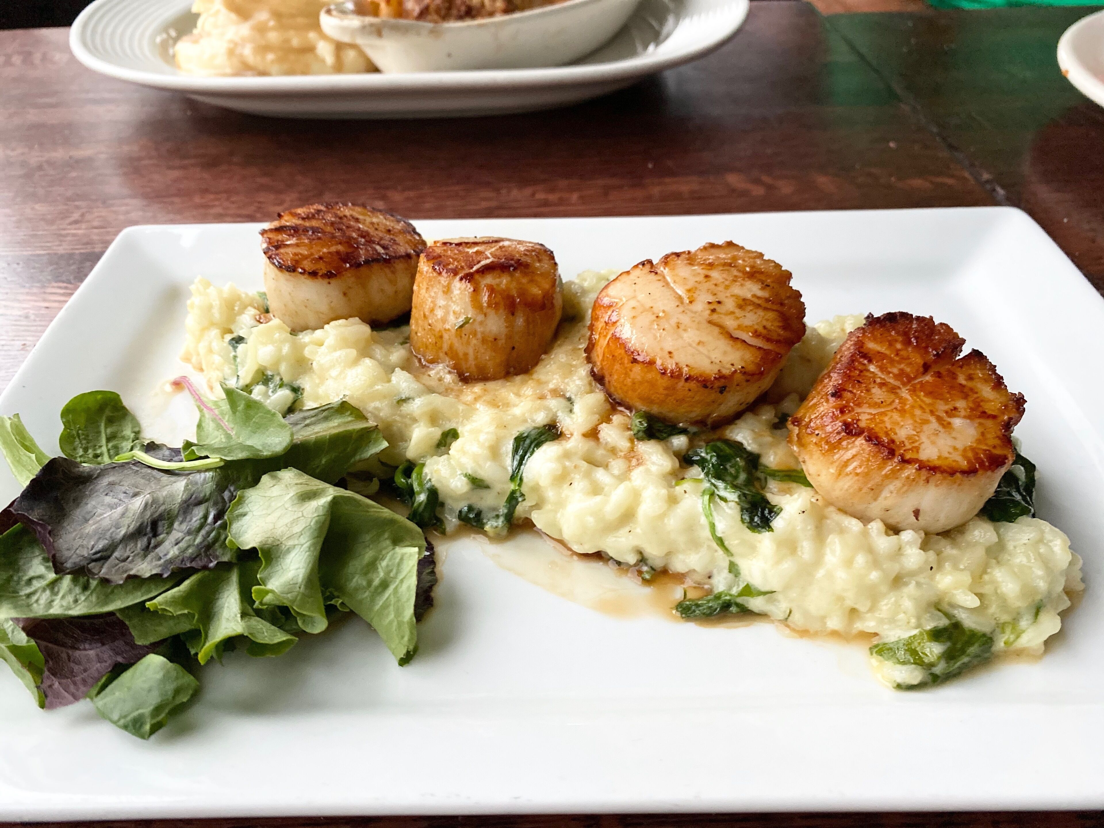 Um prato de vieiras grelhadas com risoto e uma salada.