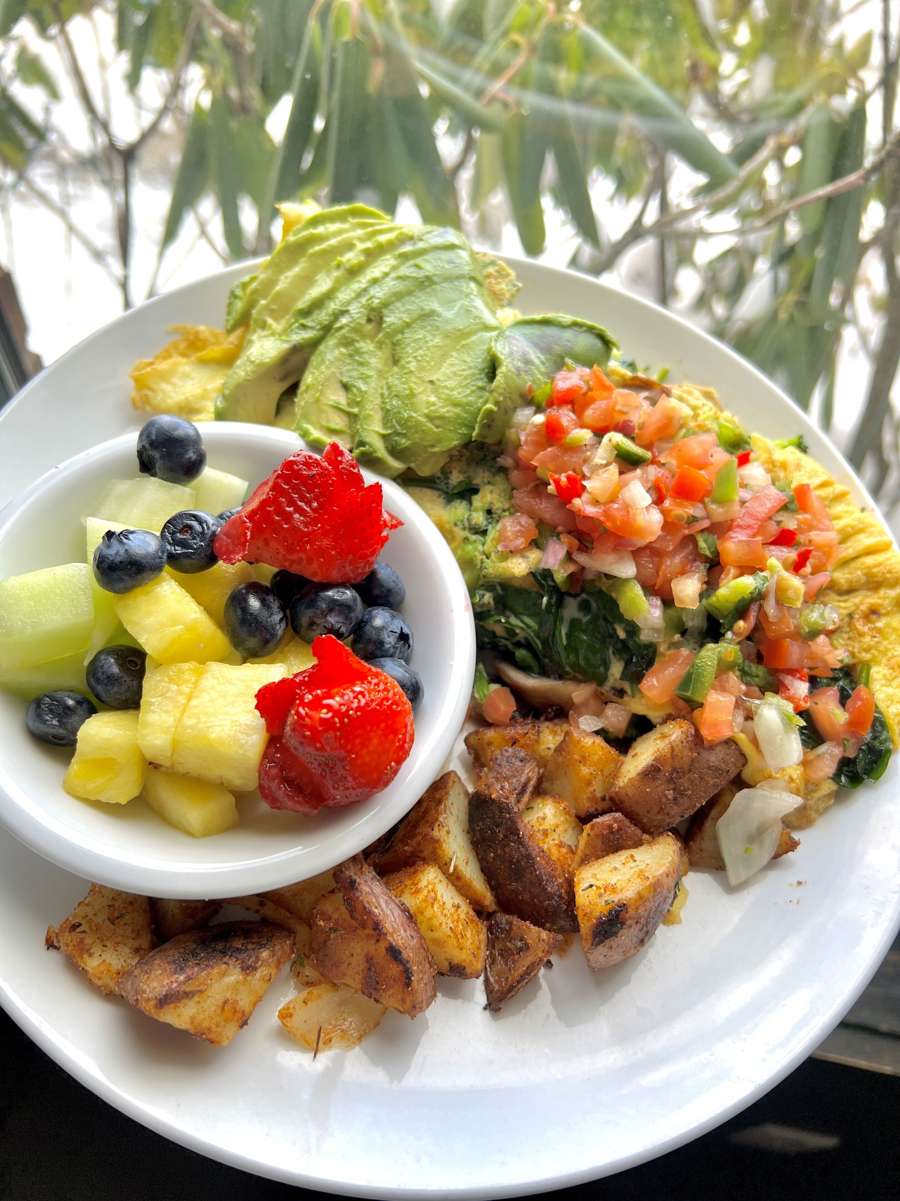 A plate of food with avocado, fruit, and a salsa.