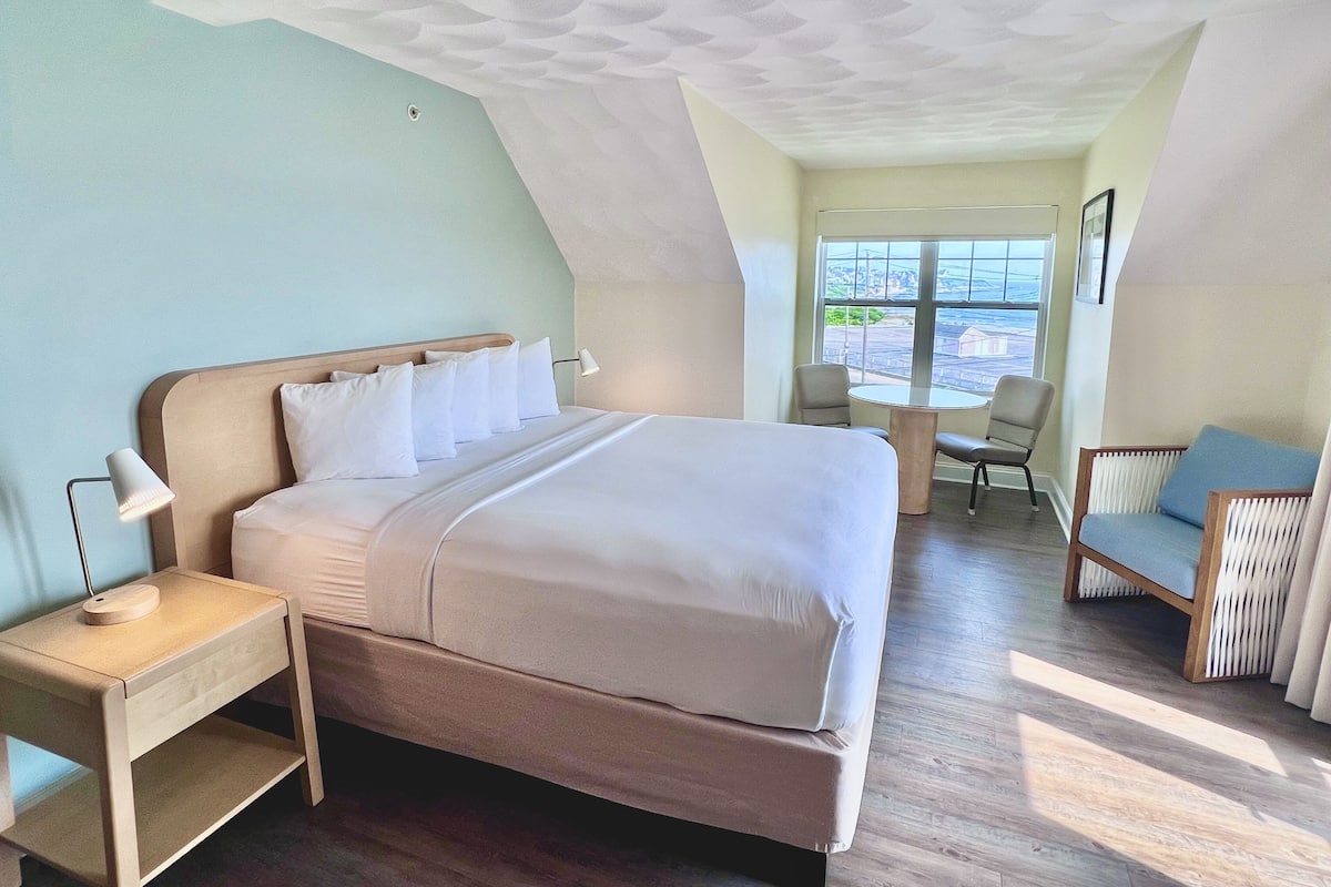 Een slaapkamer met een bed, nachtkastjes, een stoel en uitzicht op de omgeving.