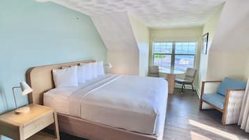 A hotel room with a bed, bedside table, lamp, and a view of the outside through a window.