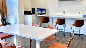 A modern meeting room with a white table and orange chairs, a computer setup, and an air conditioning unit on the wall.