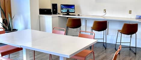 A modern meeting room with a white table and orange chairs, a computer setup, and an air conditioning unit on the wall.