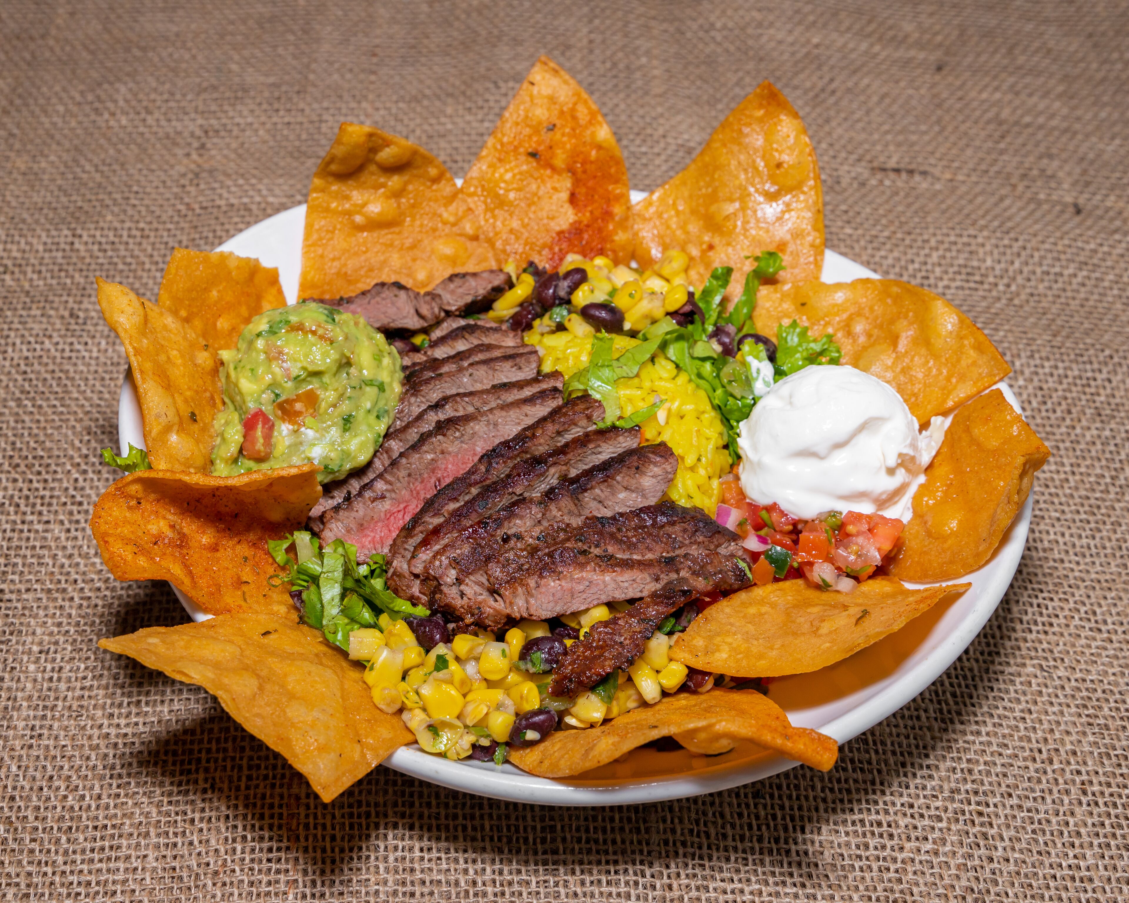 Un piatto di nachos con bistecca, mais, fagioli e guacamole.