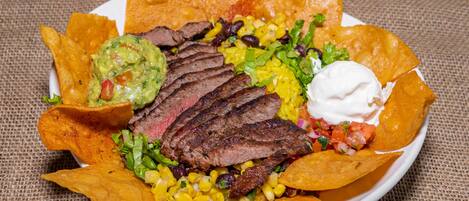 A plate of nachos with steak, corn, beans, and guacamole.