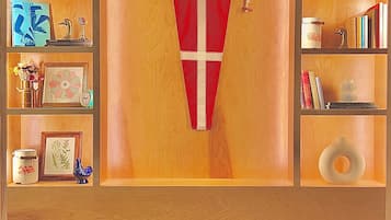 A room with a wooden door, a red and white flag, and shelves with books, decorative items, and a vase.