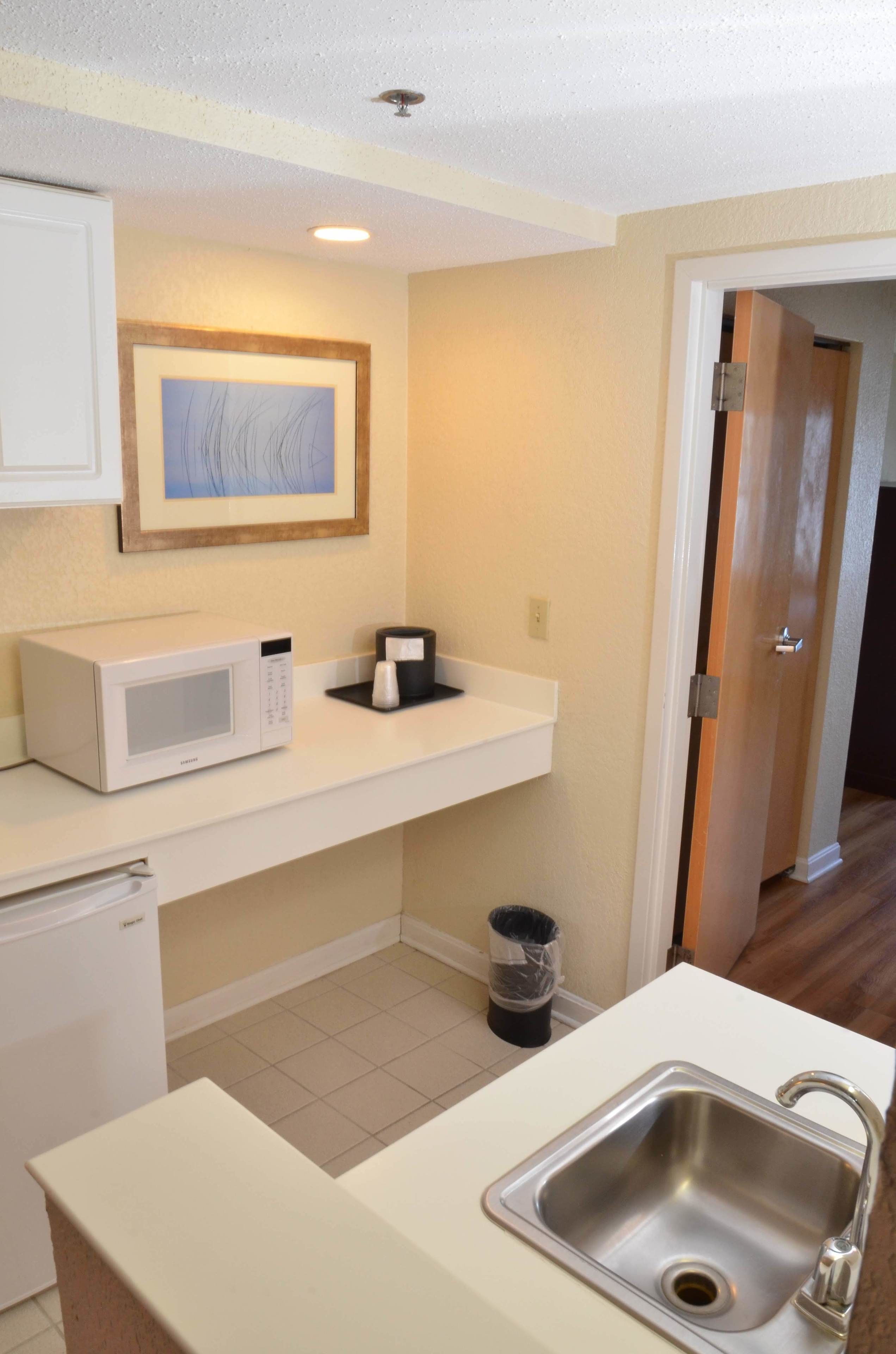 A compact kitchen with a microwave, sink, and a small trash bin.