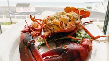 A lobster dish on a plate with a view of the sea and buildings in the background.