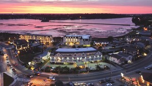 Un hôtel situé au bord de l’eau, composé de plusieurs bâtiments, doté d’un parking et bordé d’une route où circulent des véhicules.