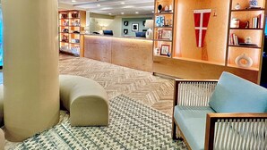 Un hall d’entrée avec un comptoir de réception, une grande colonne, un tapis à motifs et un espace détente agrémenté d’un coussin bleu.