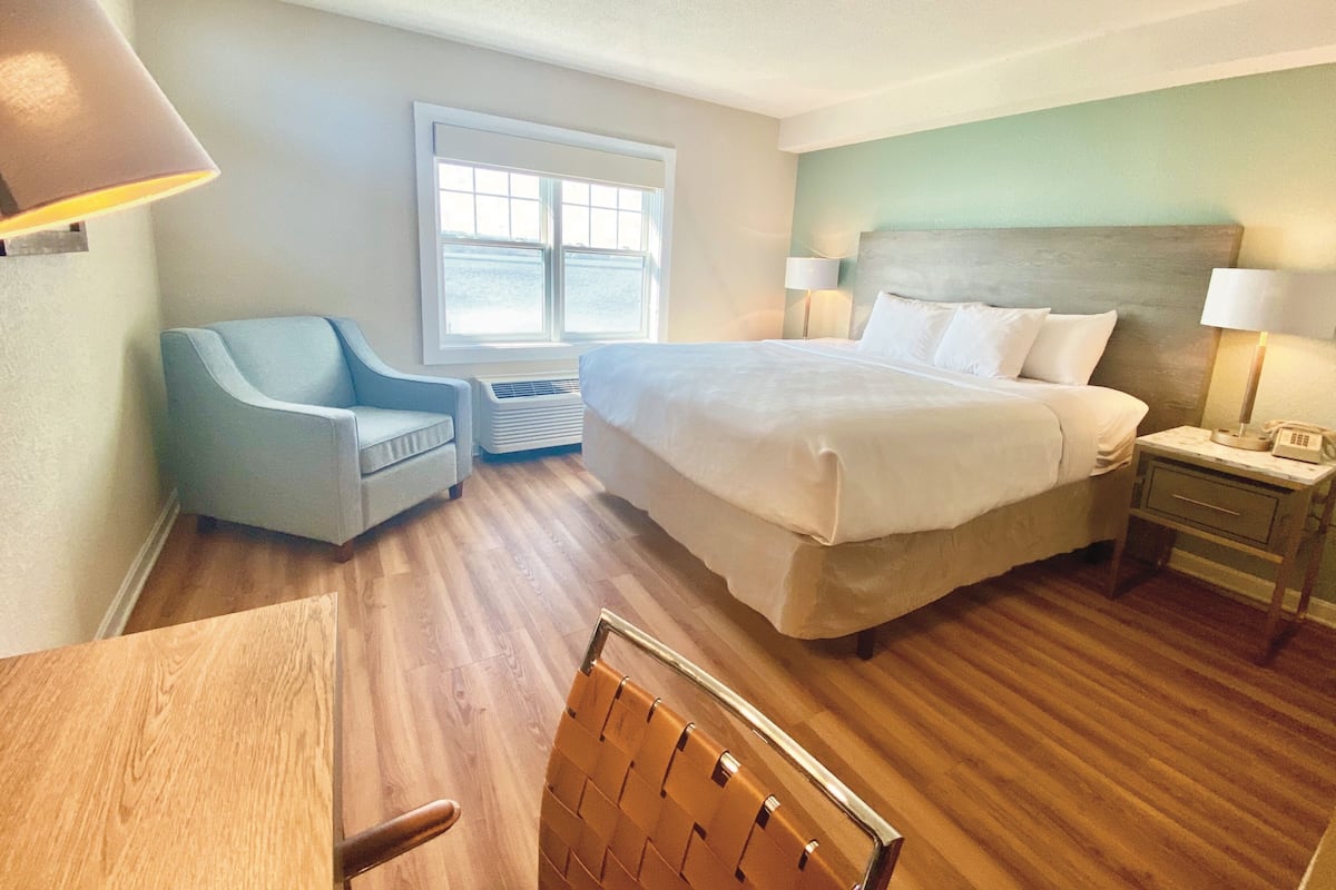 Een hotelkamer met een bed, een bureau, een stoel, een raam en een nachtkastje met een lamp.