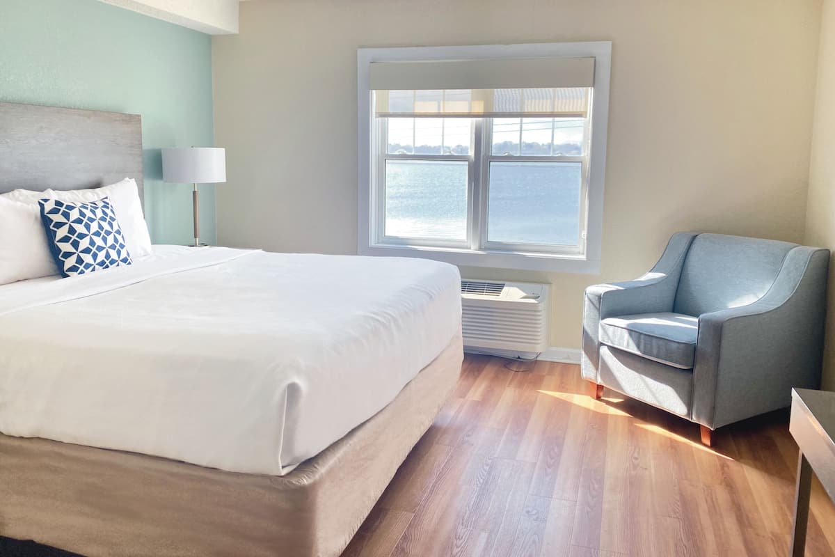 Een hotelkamer met een bed, een stoel, een raam met uitzicht op zee en een lamp.