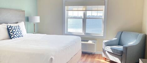 Ein Hotelzimmer mit Bett, Sessel, Fenster mit Meerblick und Lampe.