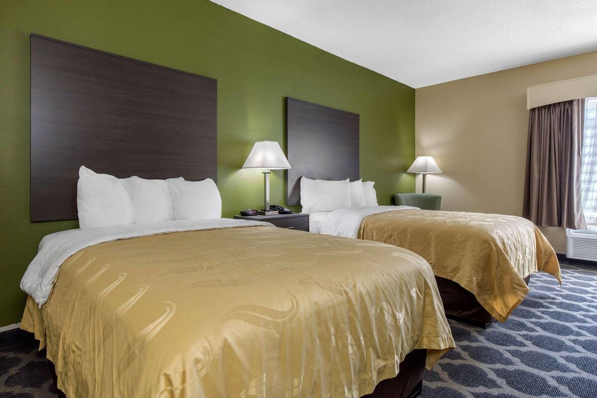 A hotel room with two beds, green walls, and a patterned carpet.