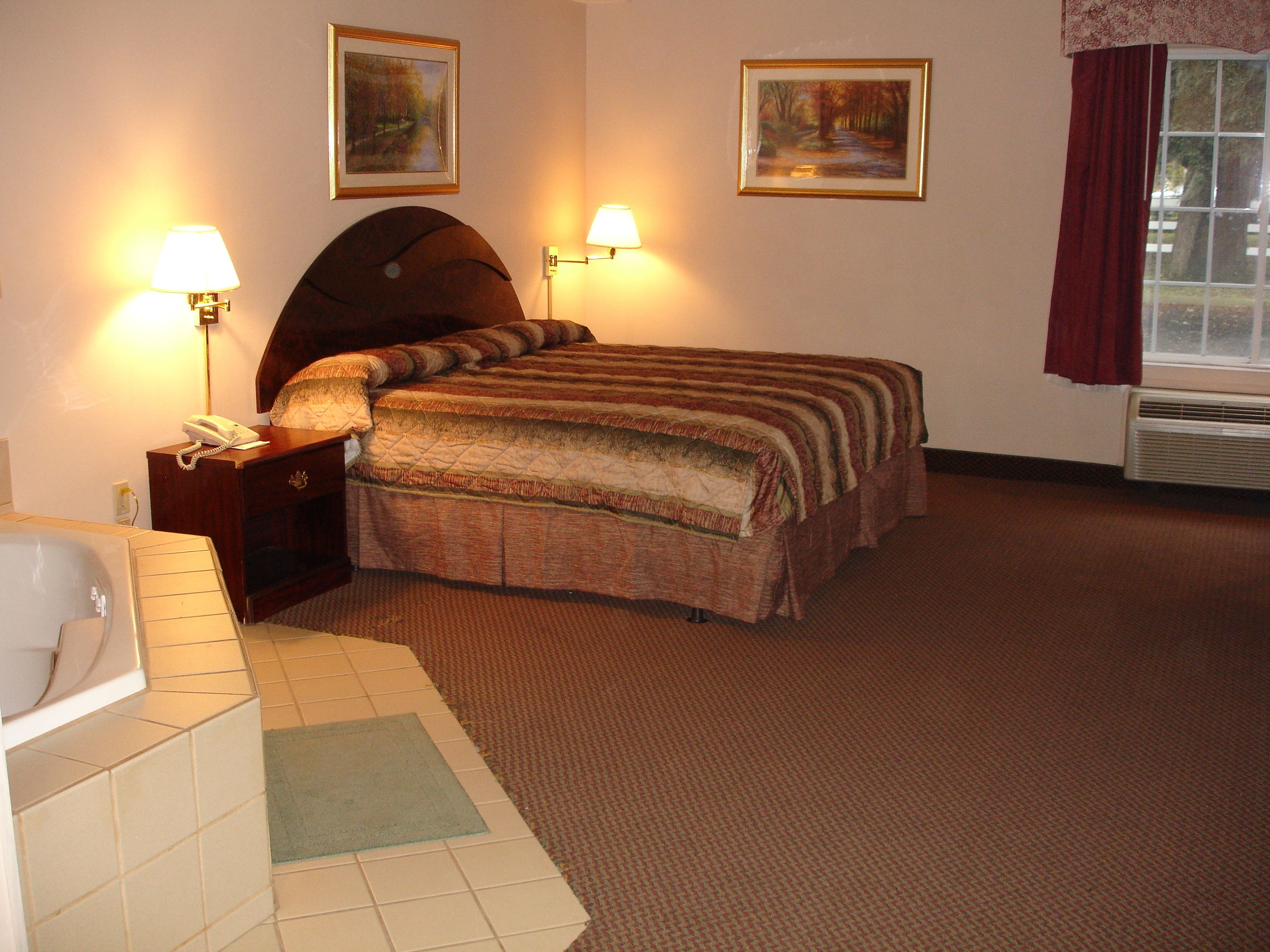 A hotel room with a bed, two wall-mounted lamps, a telephone, a window with curtains, and a radiator.