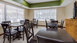A dining area with tables and chairs, large windows, and a television on a wooden cabinet. - Quality Inn Kingstree North (Kingstree)