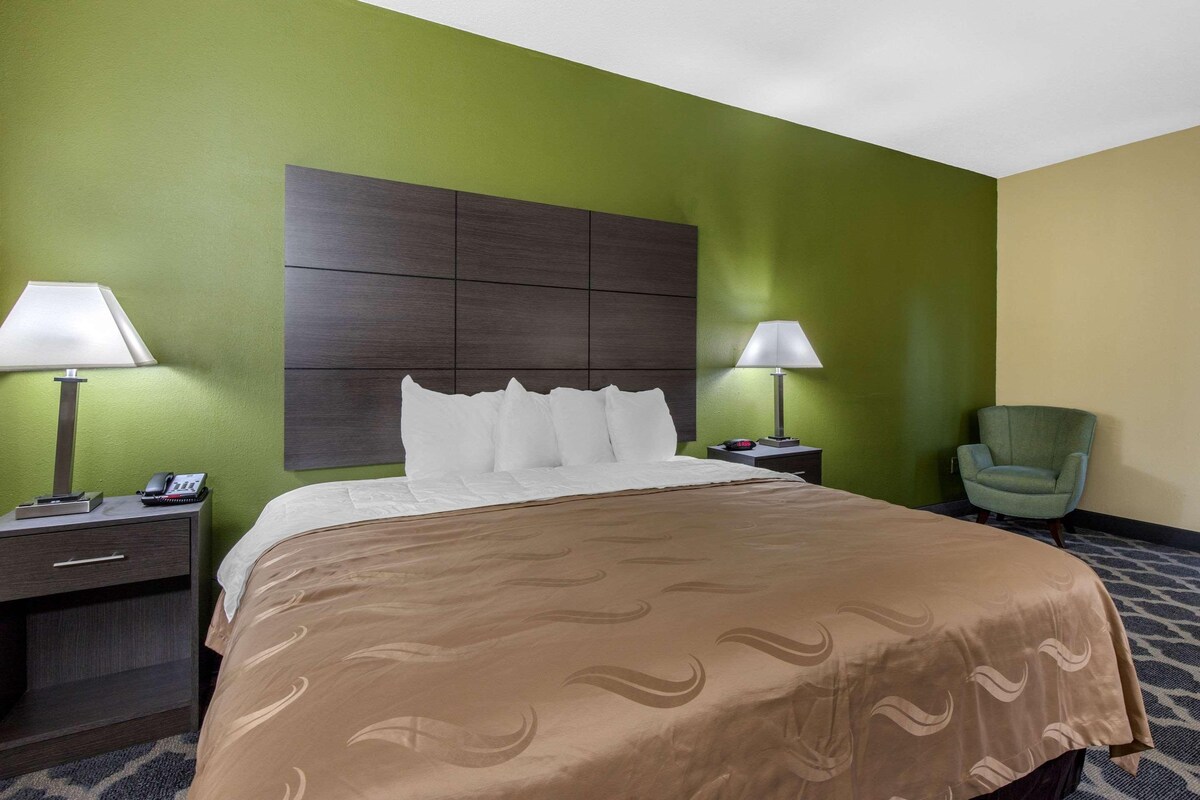 Habitación de hotel con una cama grande, dos mesitas de noche con lámparas, un sillón verde y un cabecero.