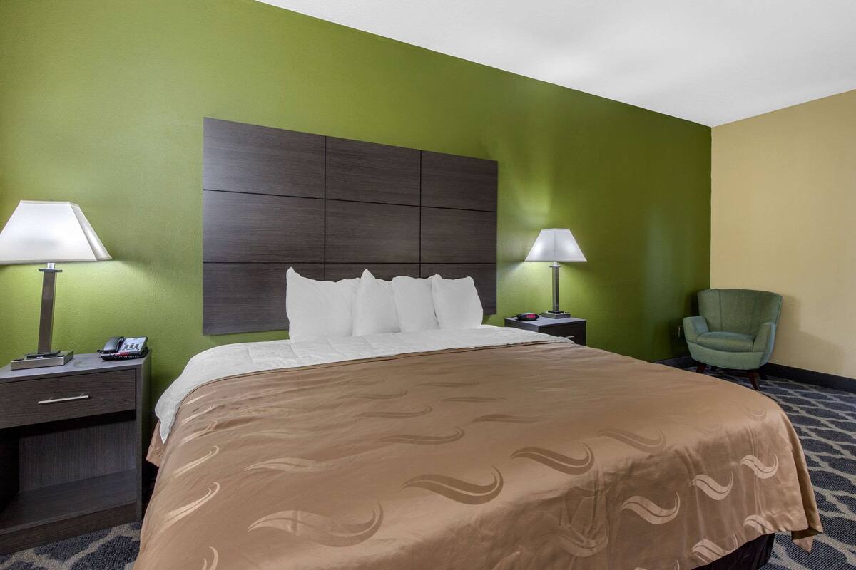 A hotel room with a bed, two bedside tables with lamps, a chair, and a headboard.
