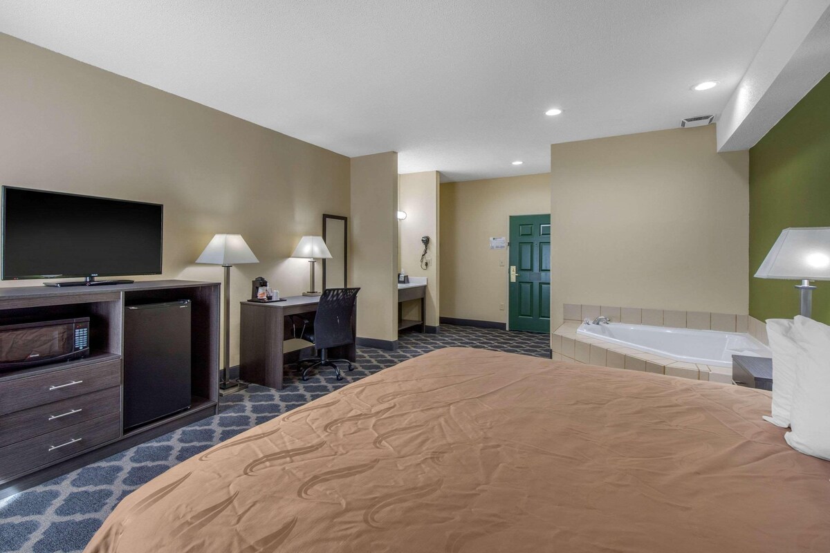 Habitación de hotel con cama, escritorio, televisor, microondas, lavabo y bañera.