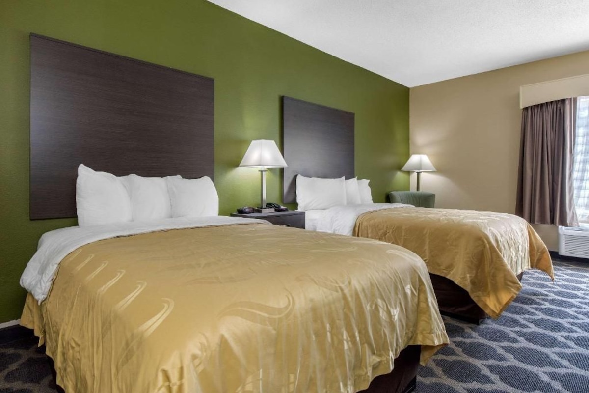 A hotel room with two beds, a large wall-mounted artwork, bedside lamps, and a window with curtains.