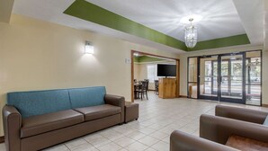 A hotel lobby with a brown sofa, a wooden reception desk, and a large window with a view of the outdoors. - Quality Inn Kingstree North (Kingstree)