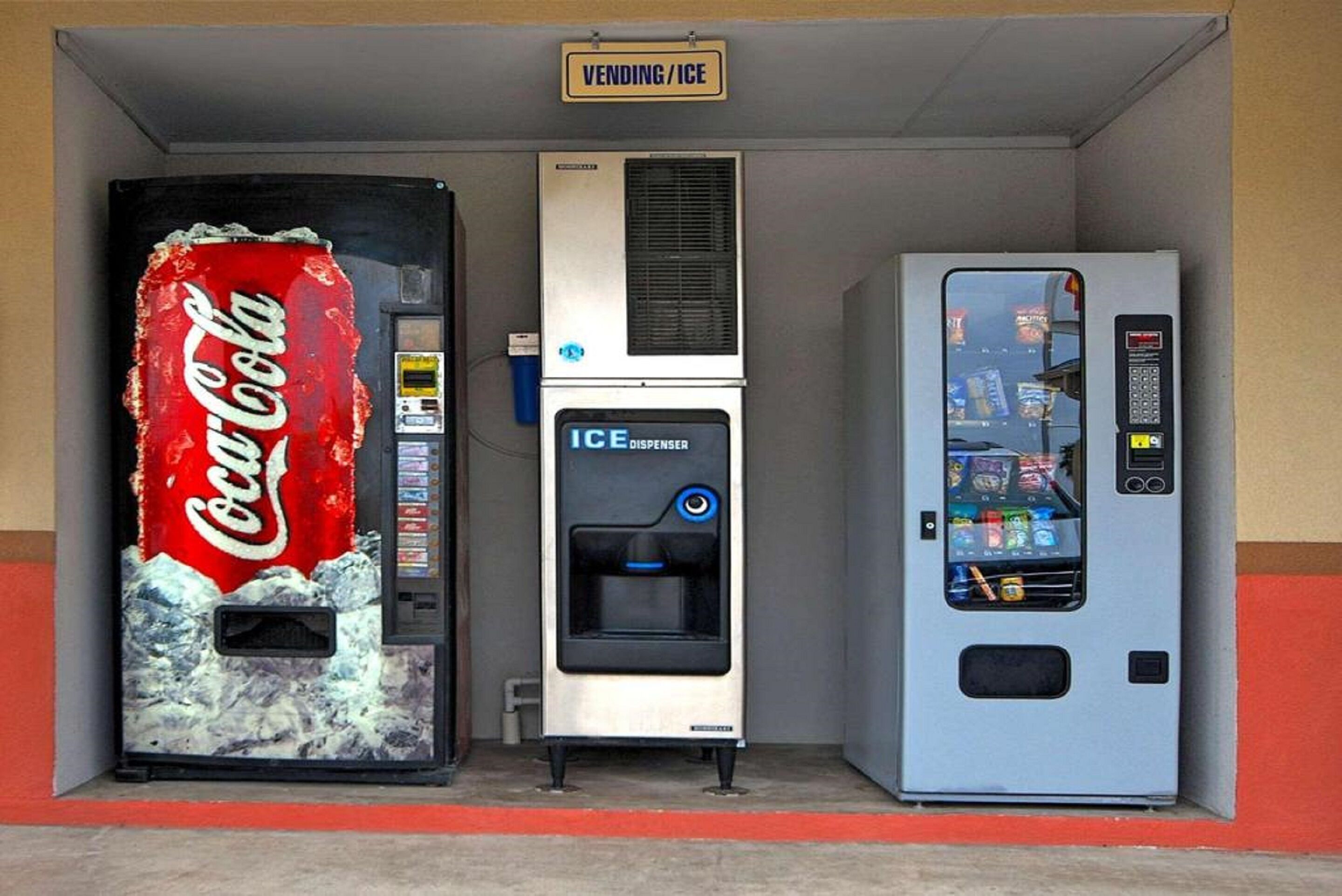 A vending machine area with a Coca-Cola branded machine, an ice dispenser, and a vending machine with various snacks.