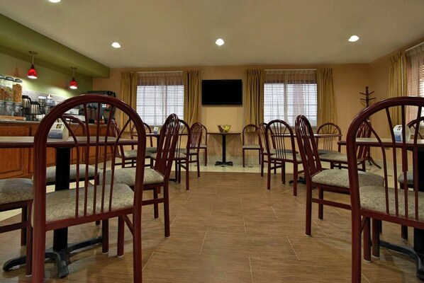 A dining area with wooden chairs and tables, a small table with a bowl, and a television on the wall.