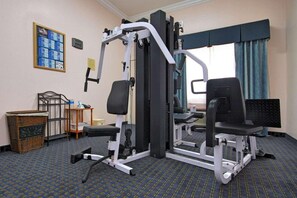 A gym with exercise equipment, a wicker basket, a small table with a bottle, and a framed picture on the wall. - Americas Best Value Inn Sinton (Sinton)