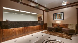 A lobby with a reception desk, two armchairs, a coffee table, a painting, and a decorative rug. - Americas Best Value Inn Sinton (Sinton)