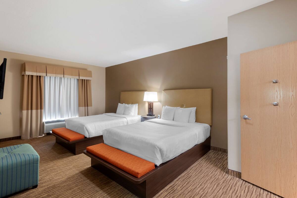 A hotel room with two beds, a desk, a chair, and a wardrobe.