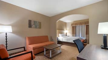 A hotel room with a bed, a sofa, a desk, and a lamp.