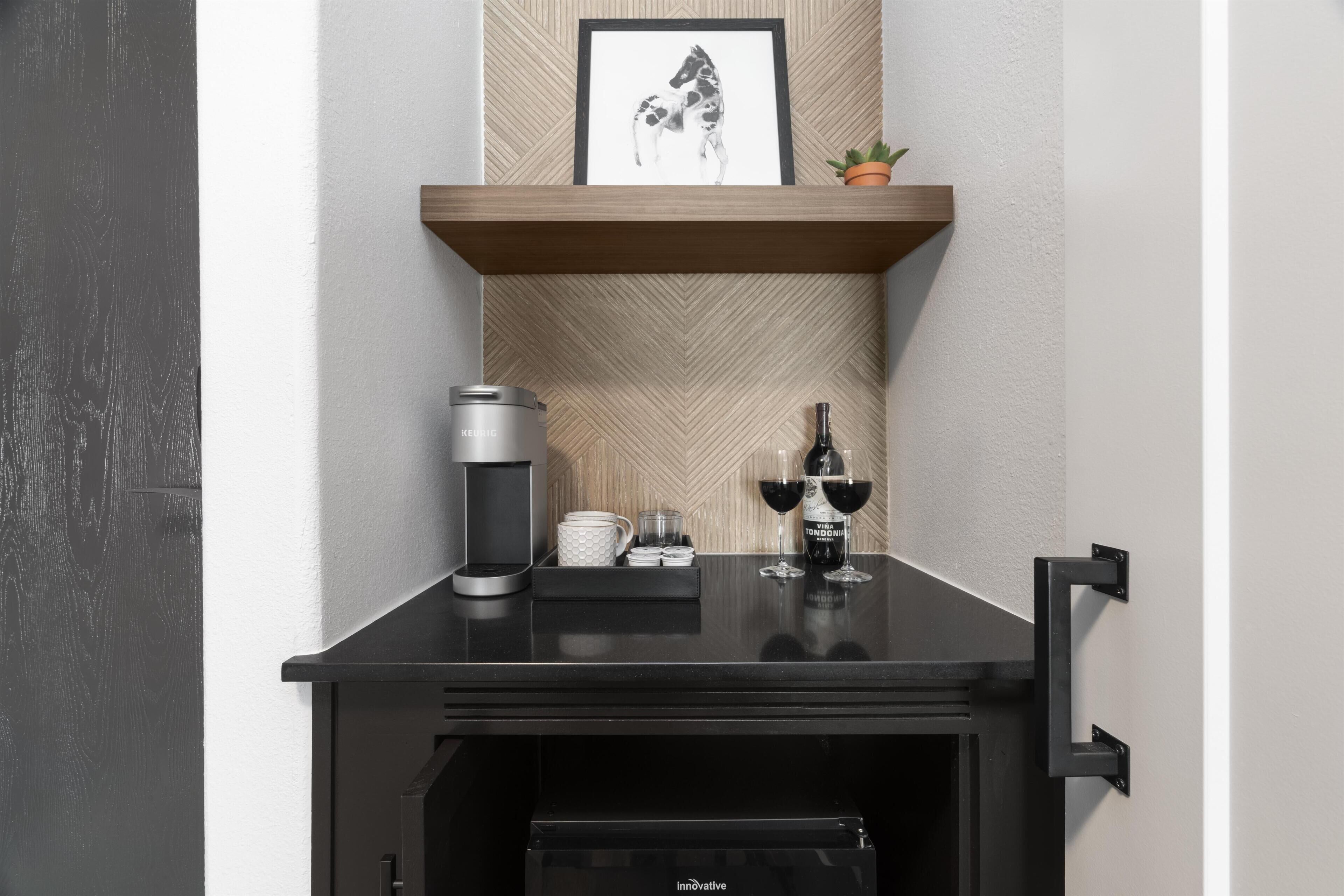 A black minibar with a coffee maker, two wine glasses, and a bottle of wine.