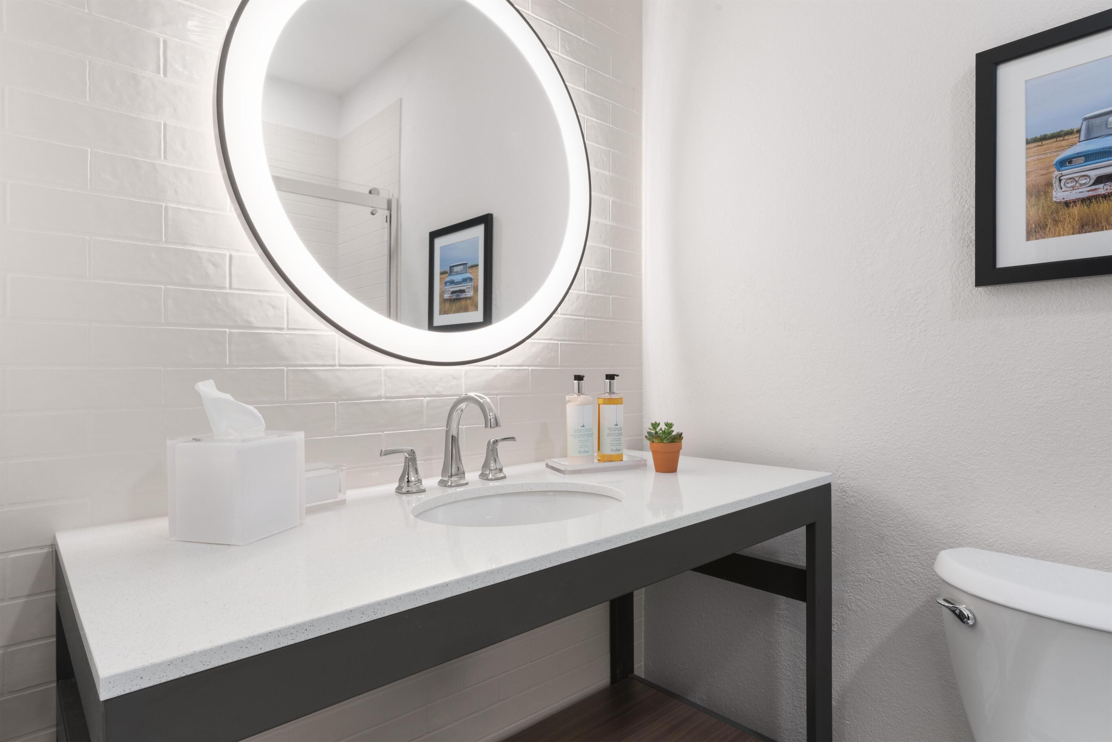 Een moderne badkamer met een witte wastafel, een ronde spiegel, een toilet en een lijst met een foto aan de muur.