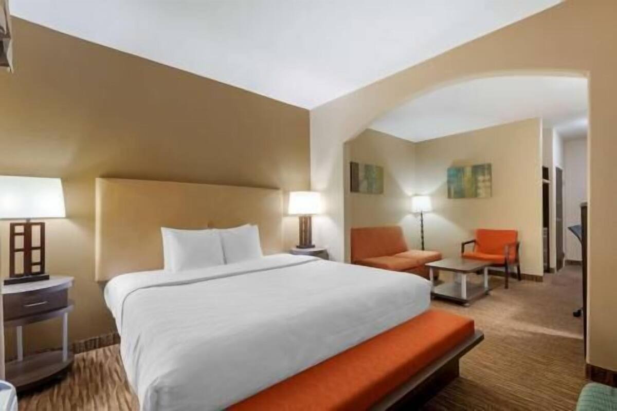 A hotel room with a bed, two chairs, a small table, and a lamp.