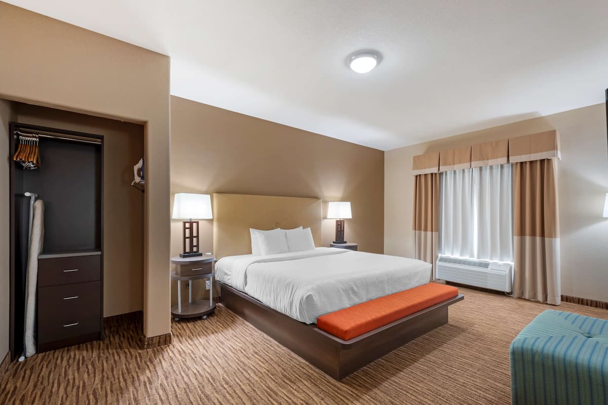 A hotel room with a large bed, bedside tables with lamps, a bench, a wardrobe, and a window with curtains.