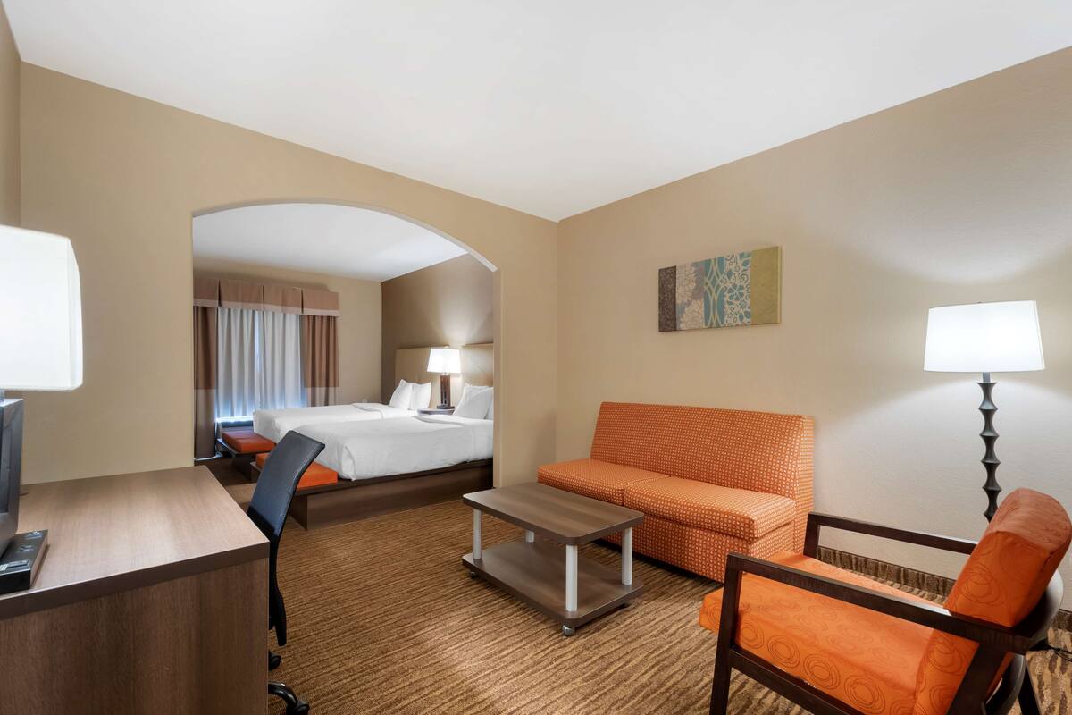 A hotel room with a bed, a desk, a chair, a sofa, and a lamp.