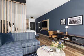 A modern living room with a sofa, a coffee table with a book and flowers, a TV mounted on the wall, and a desk with a lamp and books. - Best Western Plus DFW Airport Suites (Irving)