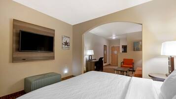 Habitación de hotel con una cama grande, un televisor de pantalla plana en la pared, un escritorio con una silla y un sillón naranja.