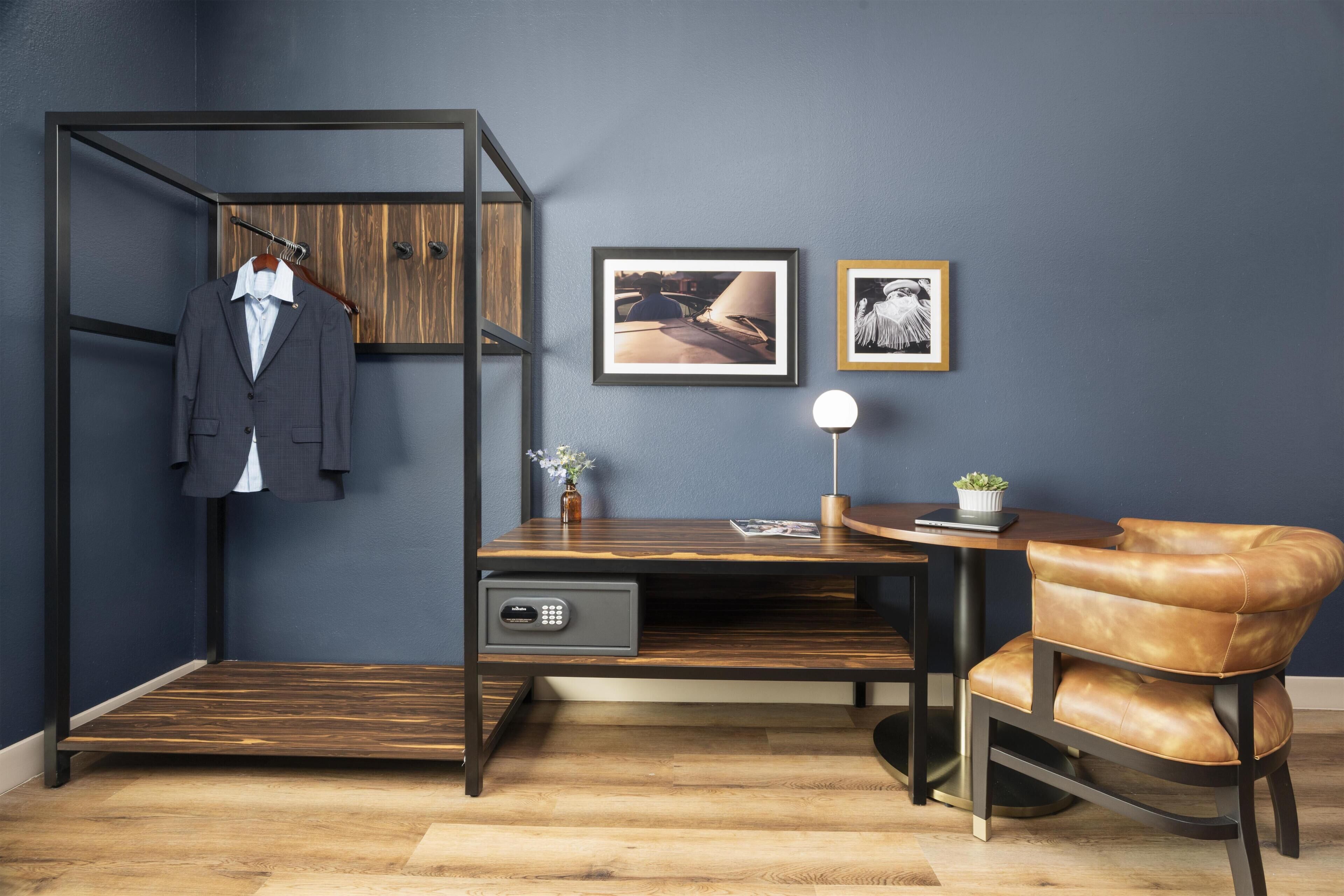 Una habitación con un armario de madera, un escritorio con una lámpara, una silla y dos cuadros en la pared.