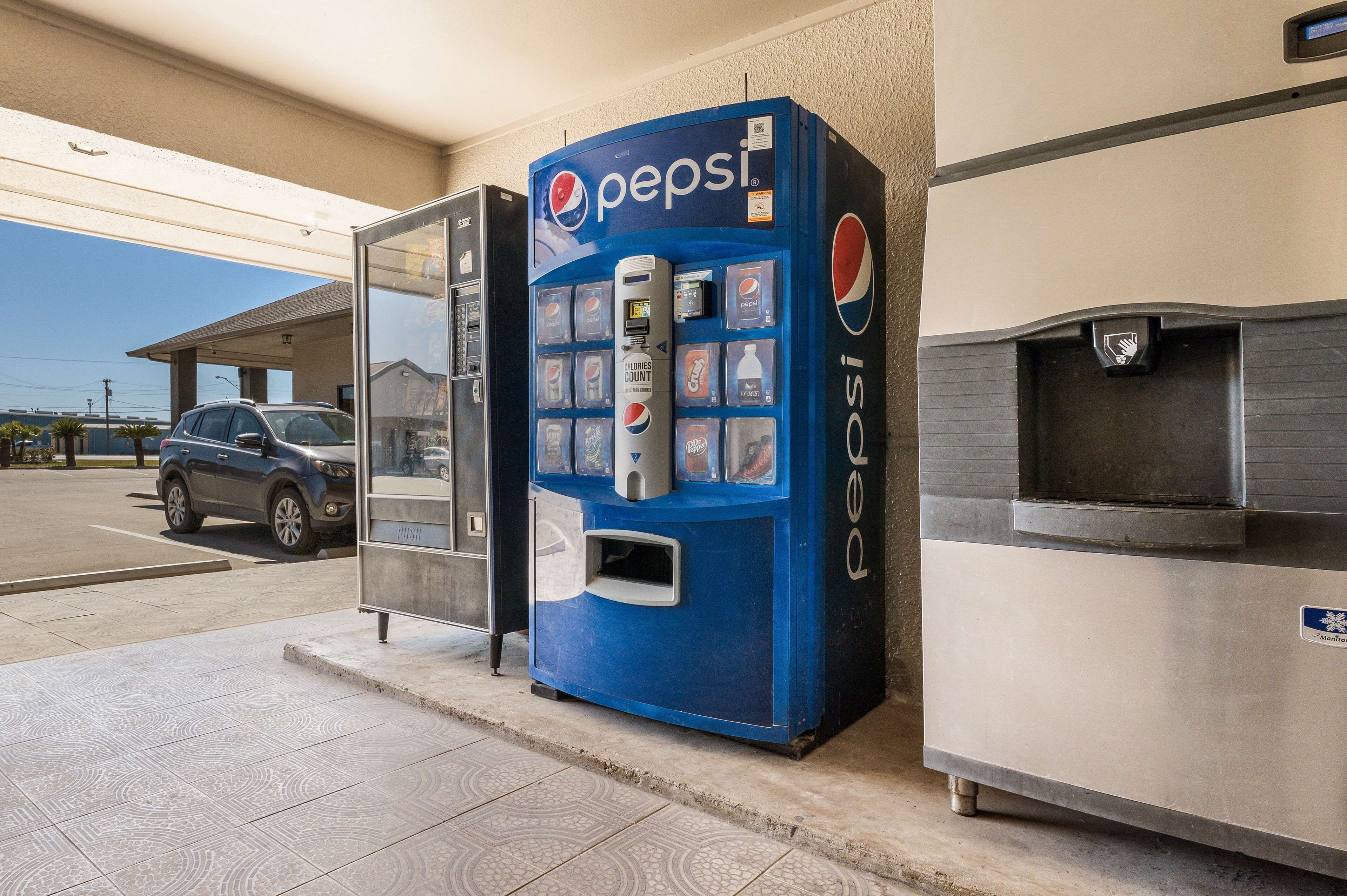 A blue Pepsi vending machine at a gas station with a car parked nearby.