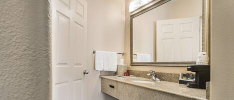 A bathroom with a white door, a sink with a mirror, and a coffee machine.
