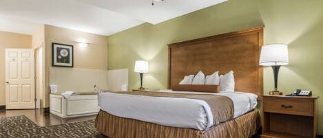 A hotel room with a bed, bedside lamps, a wooden headboard, a nightstand, a bathroom with a bathtub, and a patterned rug.