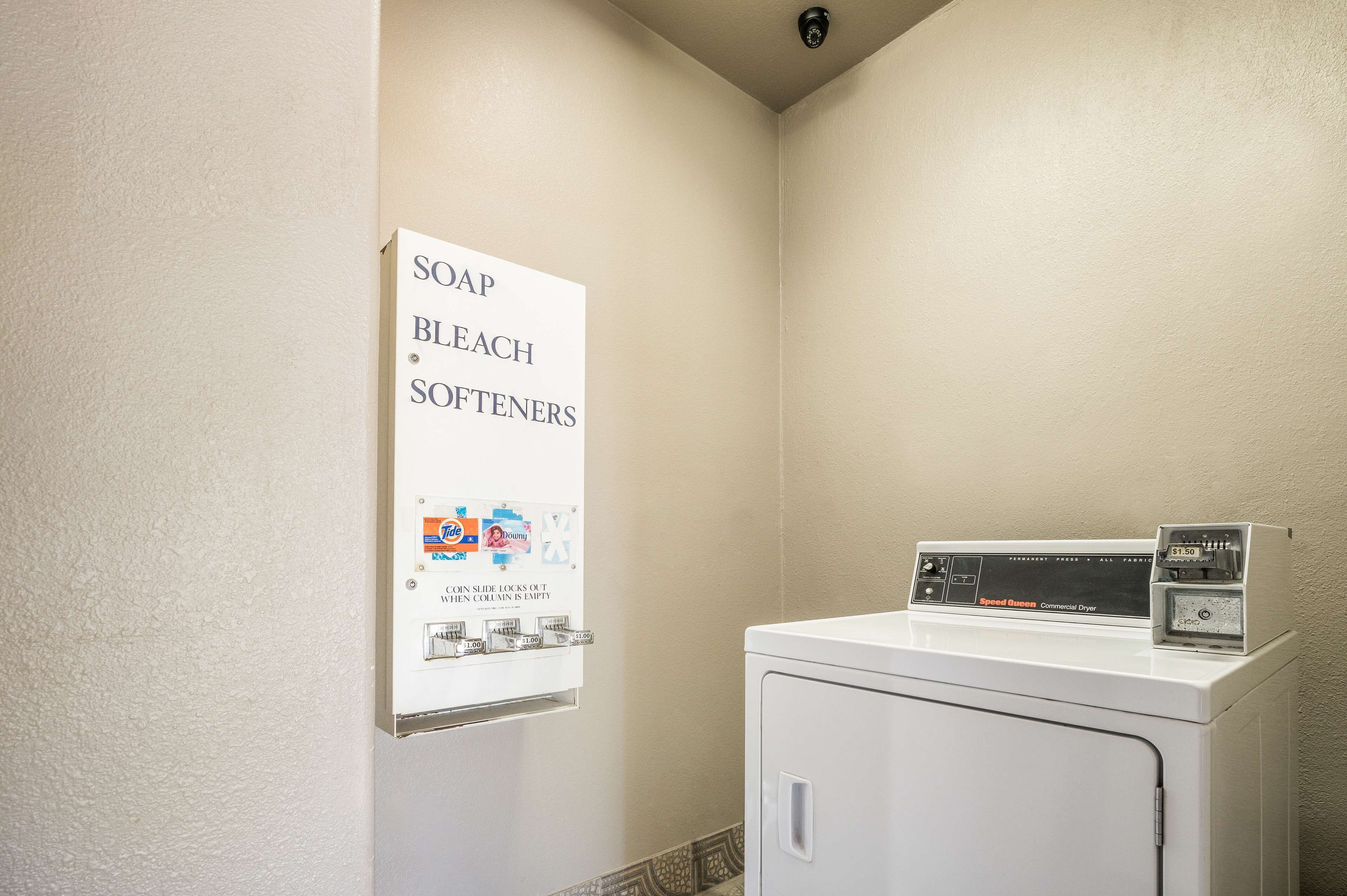 A laundry area with a commercial dryer and a soap, bleach, and softeners dispenser.