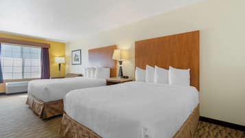 Quarto de hotel com duas camas, uma janela com cortinas, um abajur e um quadro na parede.