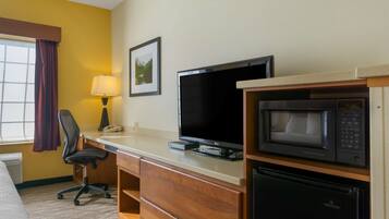 Una habitación de hotel con una cama, un escritorio con computadora, televisión, microondas y refrigerador.