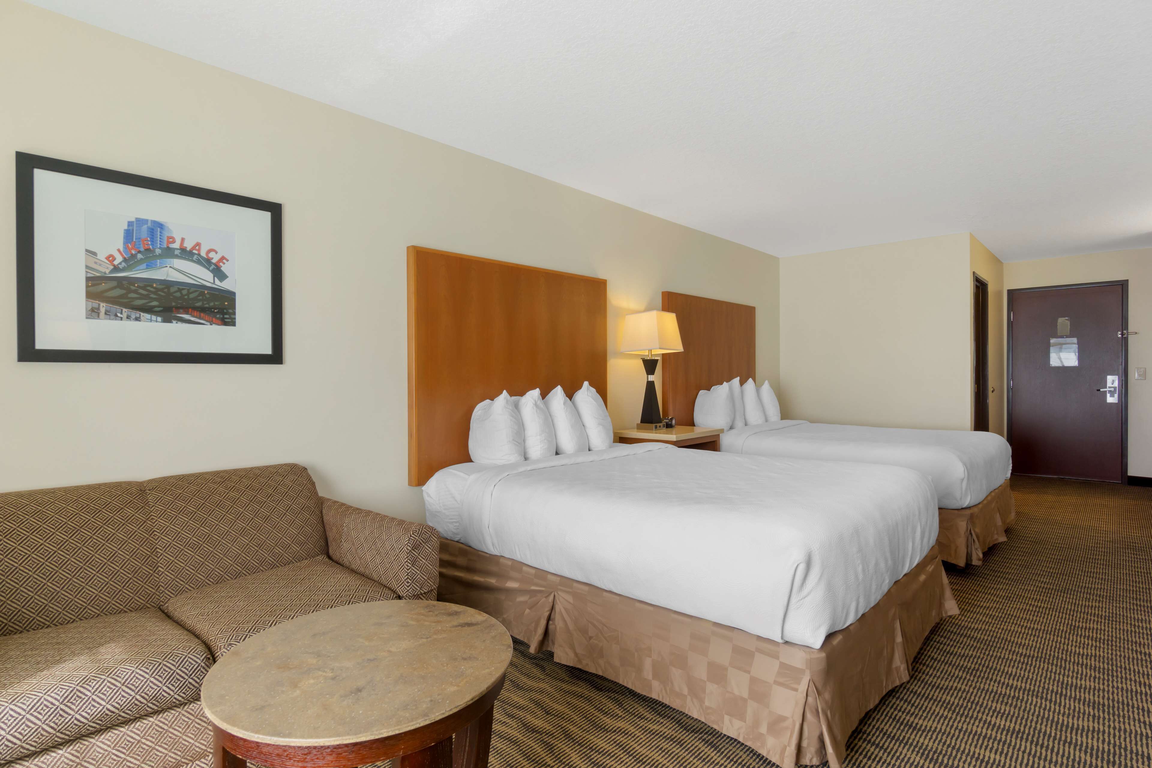 A hotel room with two beds, a sofa, a small round table, and a framed picture on the wall.