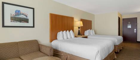 A hotel room with two beds, a sofa, a small round table, and a framed picture on the wall.